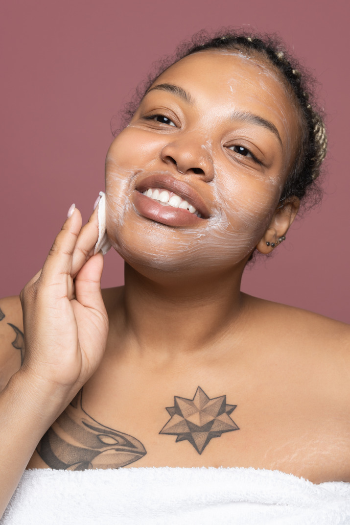 Cheerful afro woman applying face skin product with cotton pad