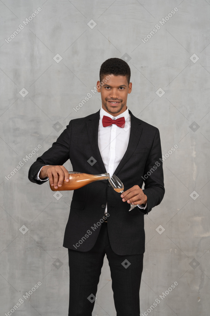 Homme souriant remplissant un verre de flûte et regardant la caméra
