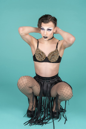 Drag queen squatting with hands behind their head