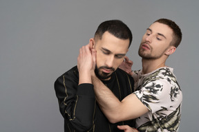 Young caucasian man holding another man sensually by the neck in a half-hug