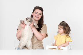 Mom sitting next to a daughter in children's chair and holding a cat