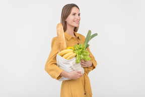 Dreamy young woman holding shopping bag with vegetables and baguette
