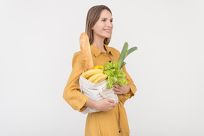 Giovane donna sognante tenendo la borsa della spesa con verdure e baguette