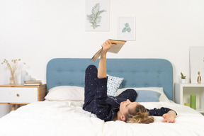 Pleine longueur d'une jeune femme ennuyée essayant de lire un livre au lit