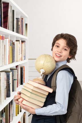 A young boy holding a stack of books in front of a bookshelf