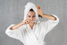 Mujer en bata de baño exprimiendo pasta de dientes fuera del tubo