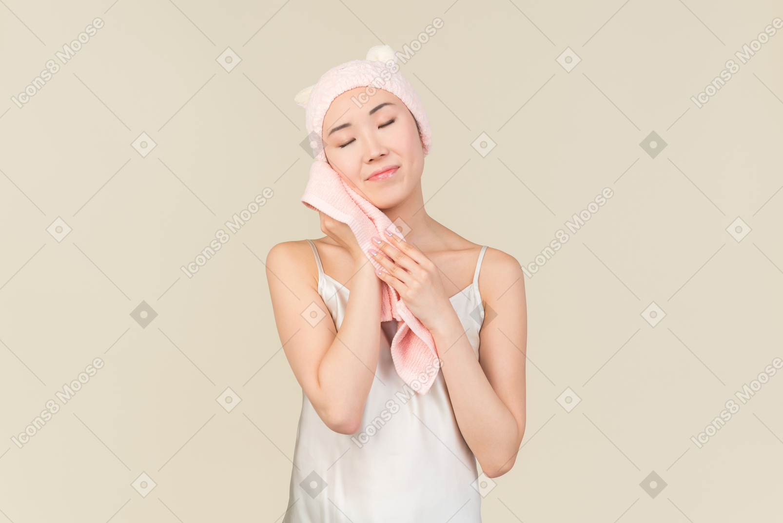 Young asian woman in pink rabbit hat with eyes closed drying face with pink towel