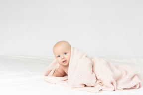 Smiling baby boy covered in beige knitted blanket