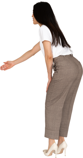 Vista laterale di una giovane donna in calzoni e t-shirt allungando la mano e chinandosi