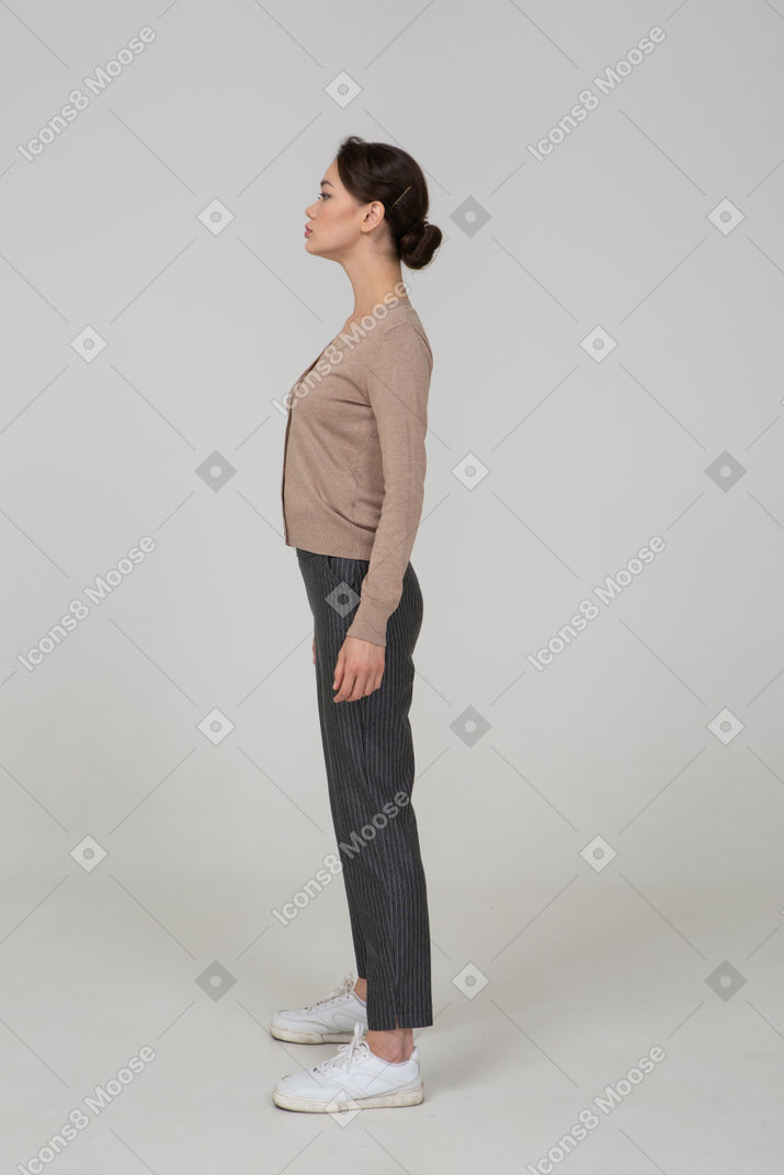 Side view of a young lady standing still in pullover and pants looking aside