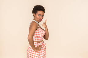Joven mujer negra de pelo corto con un top a cuadros y una falda, posando sobre un fondo liso color melocotón