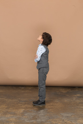 Vista lateral de um menino de terno cinza, abraçando-se
