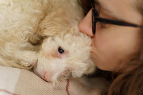 Close-up de uma jovem mulher de óculos beijando seu pequeno poodle