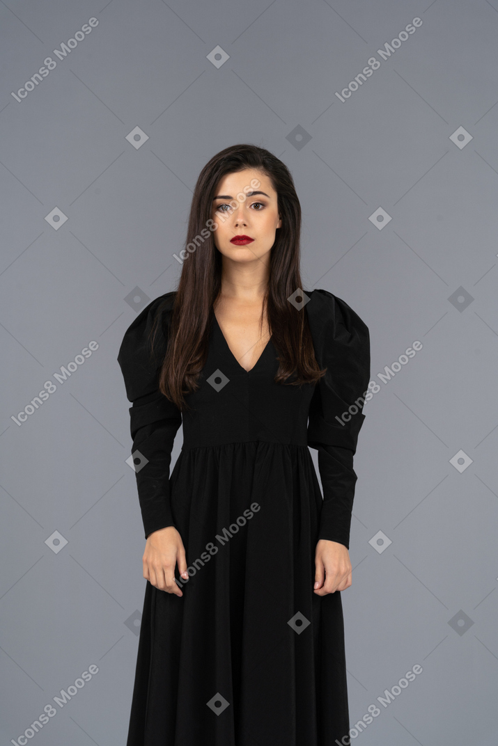Vista frontale di una giovane donna in un abito nero in piedi ancora