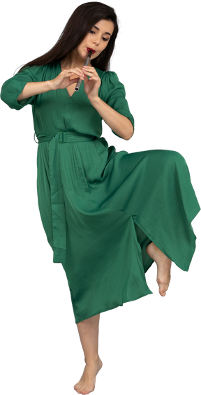 Вид спереди танцующей молодой леди в зеленом платье, играющей на флейте