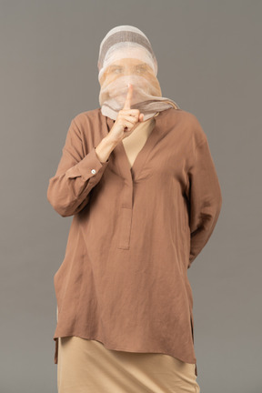Woman covered with shawl showing a silence gesture