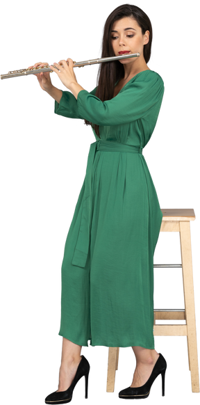 クラリネットを演奏しながら椅子に座っている緑のドレスを着た若い女性のフルレングス