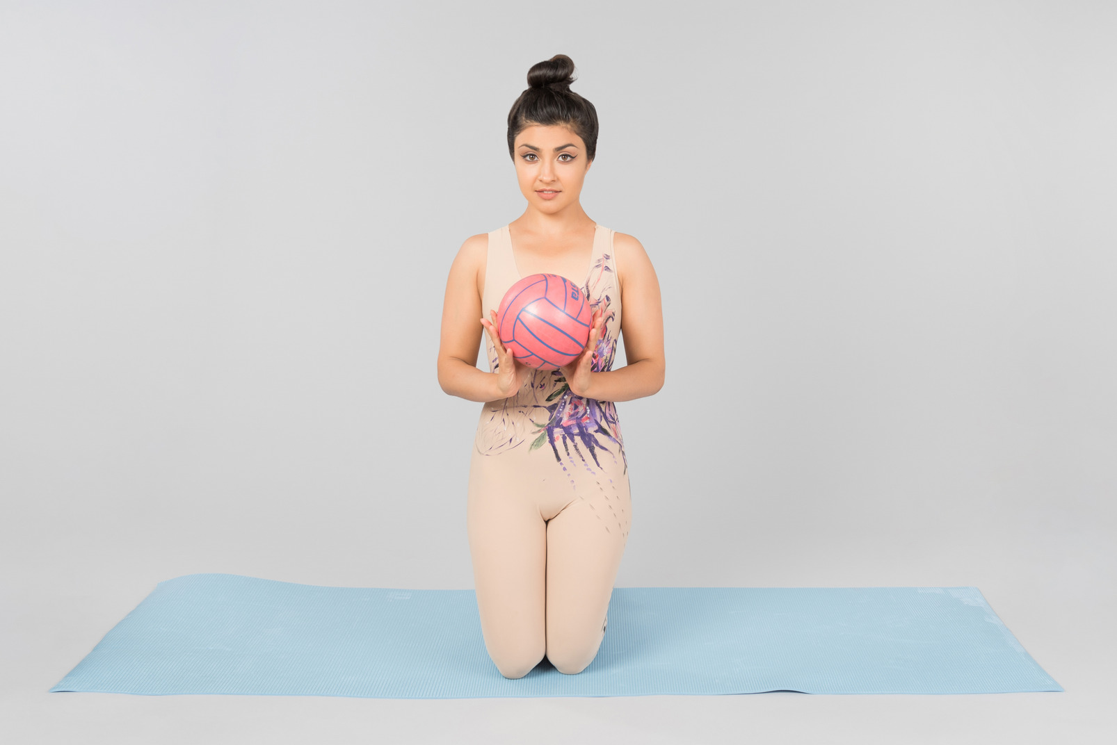 Young indian gymnast sitting on yoga mat and holding ball