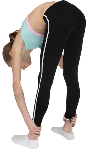 Vista posterior de tres cuartos de una jovencita en ropa deportiva estirando mientras sujeta los tobillos