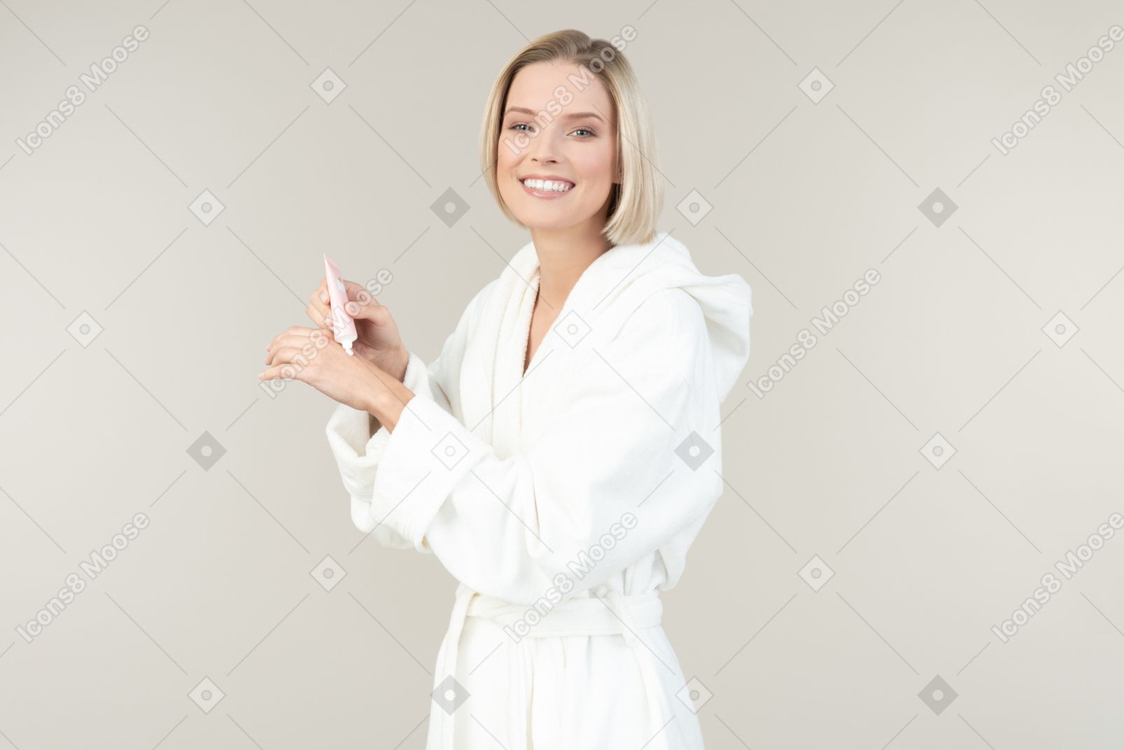 Giovane donna bionda in un accappatoio bianco in posa con tutti i tipi di articoli da toeletta
