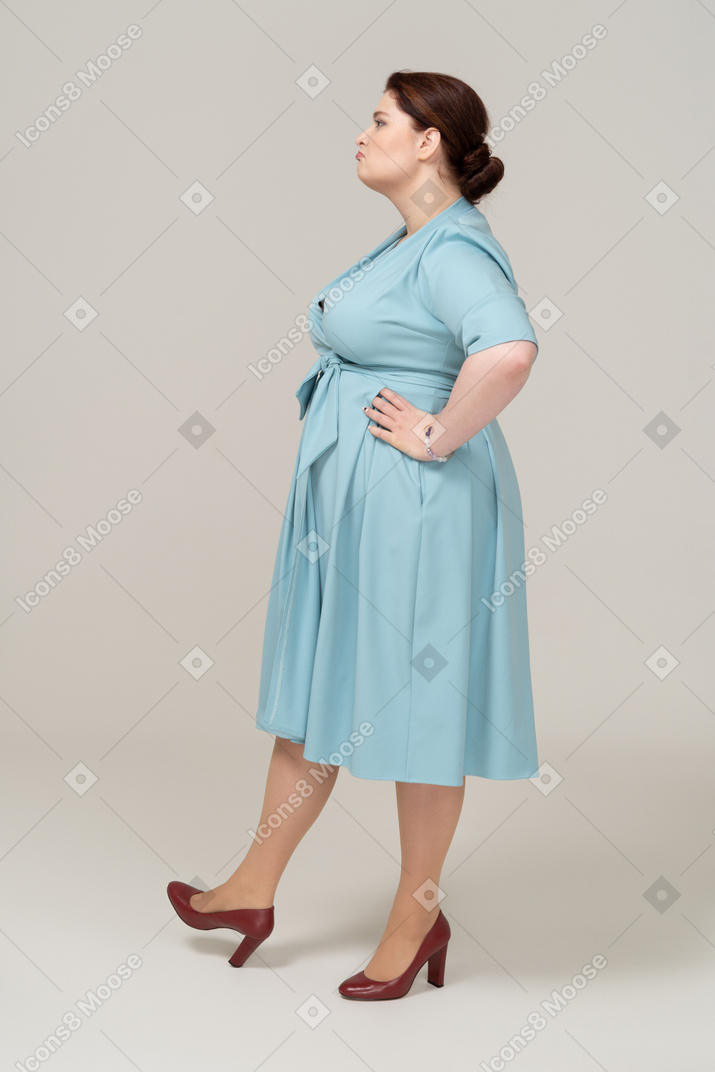 Side view of a woman in blue dress posing with hands on hips