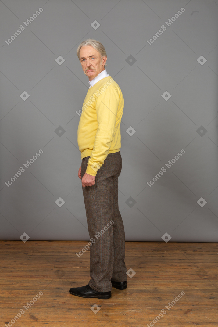 カメラを見て黄色のプルオーバーで不機嫌な老人の側面図