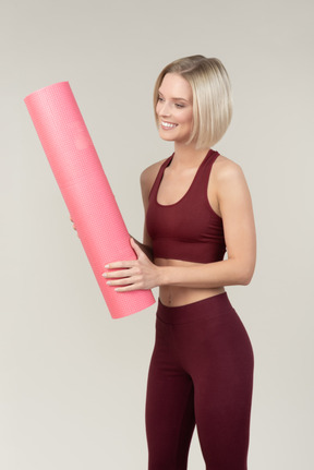 Sonriente mujer joven en ropa deportiva con estera de yoga