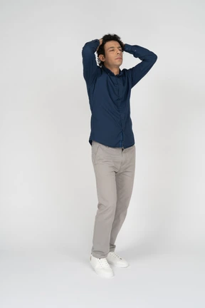 Front view of a man in casual clothes standing with hands behind head