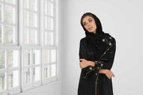 A woman wearing a black hijab standing in front of a window