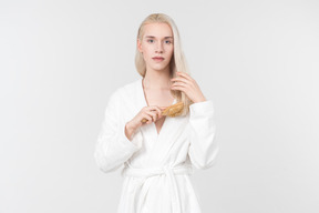 흰색 목욕 가운을 입고 머리를 빗고 있는 젊은 여자