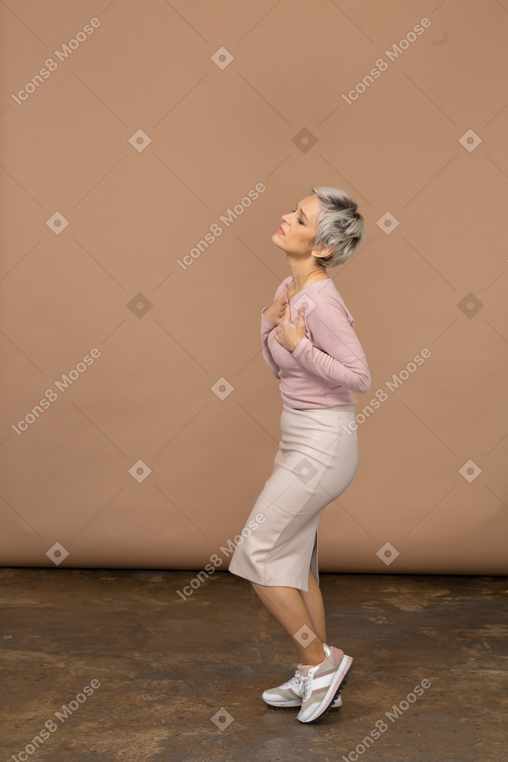 Vista laterale di una donna emotiva in abiti casual in piedi con le mani sul petto