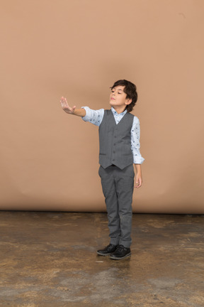 Vue de face d'un garçon mignon en costume gris debout avec le bras tendu