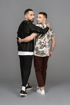Back view of two young men walking and half-hugging while looking over their shoulders
