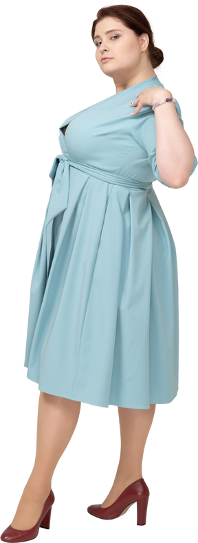 Side view of a woman in blue dress posing with hands on shoulders