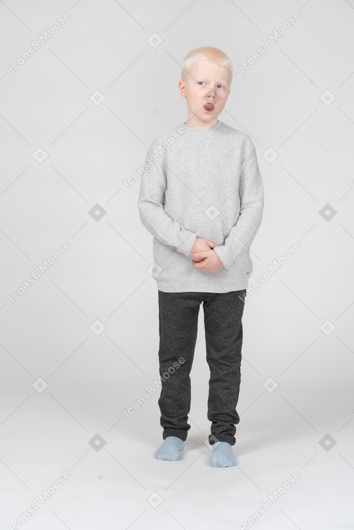 Front view of a suspicious kid boy looking aside and showing tongue