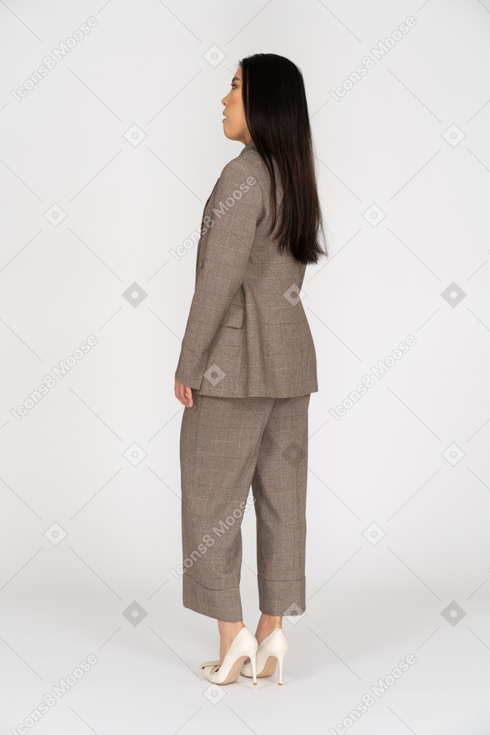 Vista traseira de três quartos de uma jovem descontente em um terno marrom olhando para o lado