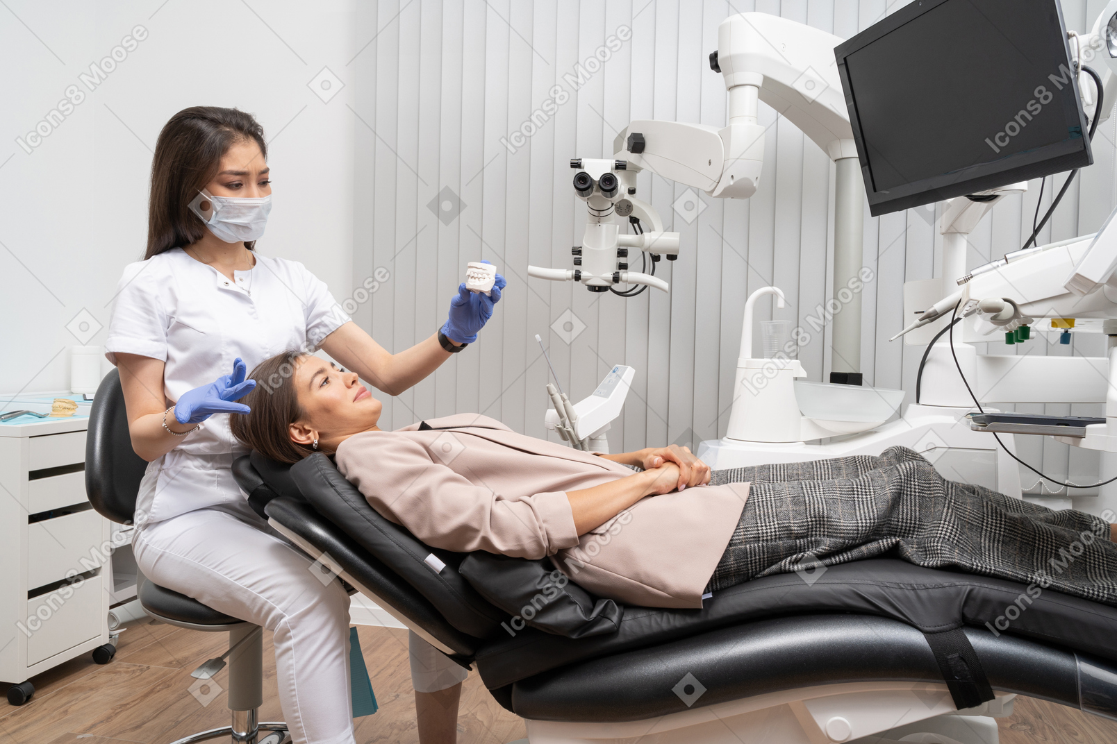 Full-length of a female dentist and her female patient looking at teeth model
