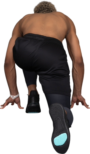 Vista posterior de un velocista de piel oscura sin camisa listo para correr