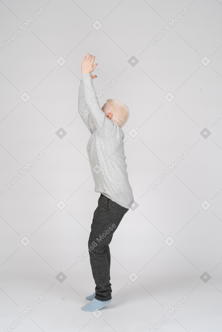 Vista laterale di un ragazzo che cerca di saltare con le mani alzate