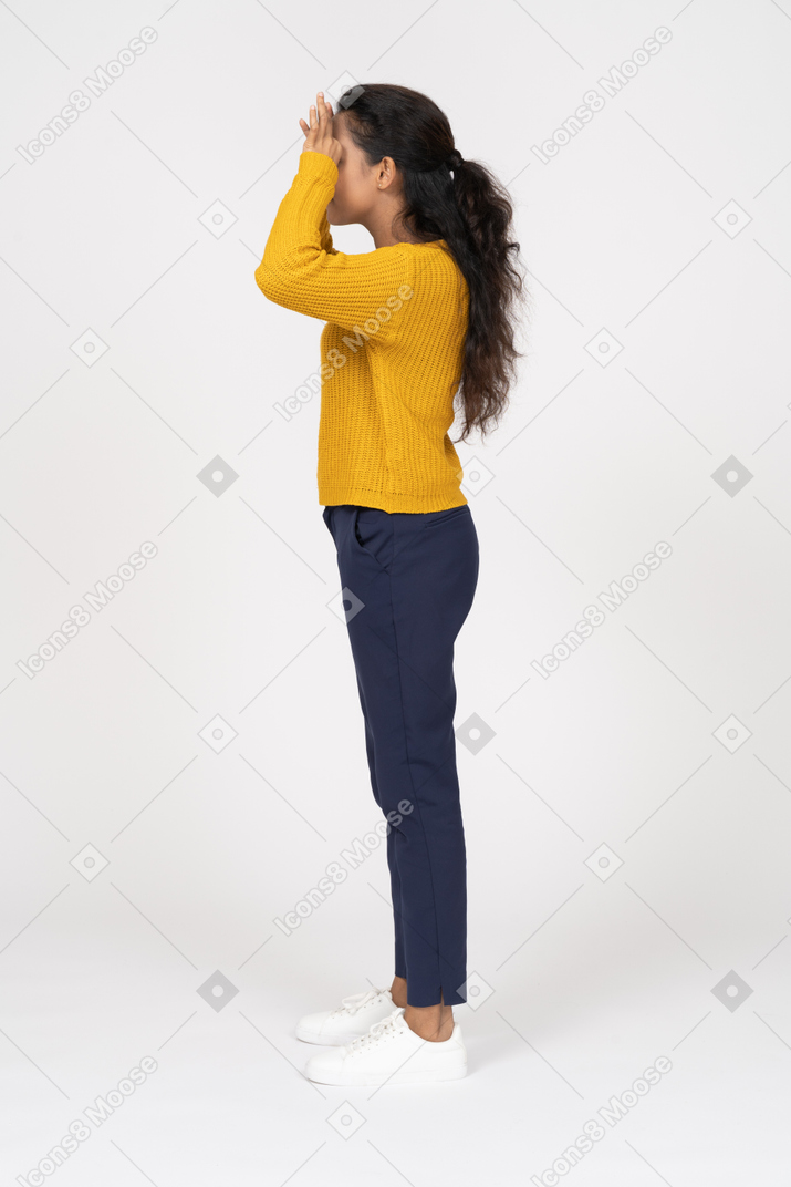 Vista lateral de una niña en ropa casual mirando a través de los dedos
