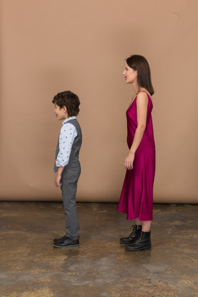 Mujer disgustada en vestido rojo y niño de pie de perfil