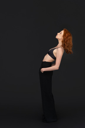 A side view of the sexy young woman standing on the black background with the eyes closed