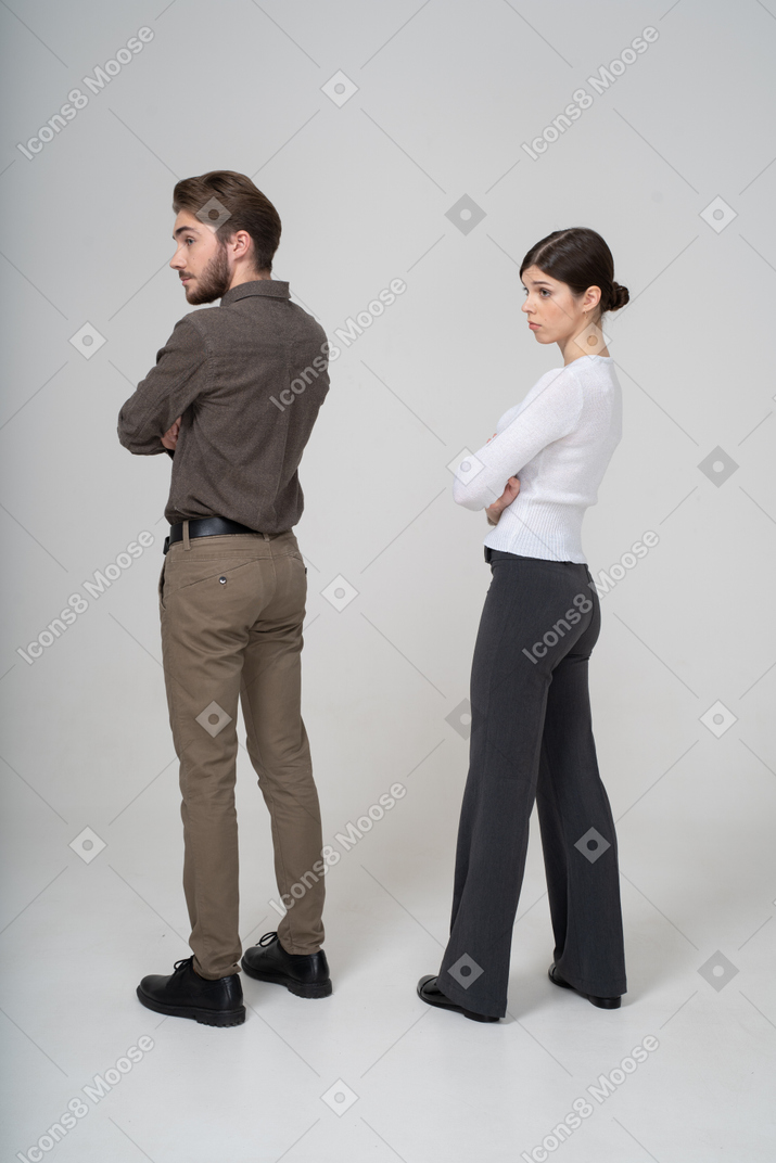 Трехчетвертный вид сзади молодой пары в офисной одежде, скрещивающей руки
