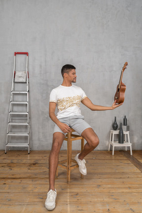 Front view of a man on a stool holding an ukulele like hamlet skull