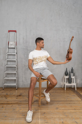 Vista frontal de um homem em um banquinho segurando um ukulele como crânio de aldeia