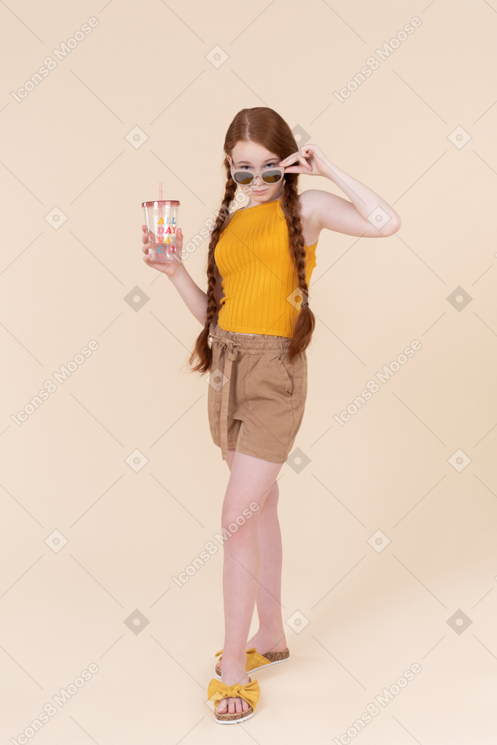 Stylish teenager girl looking over eyeglasses and holding plastic cup