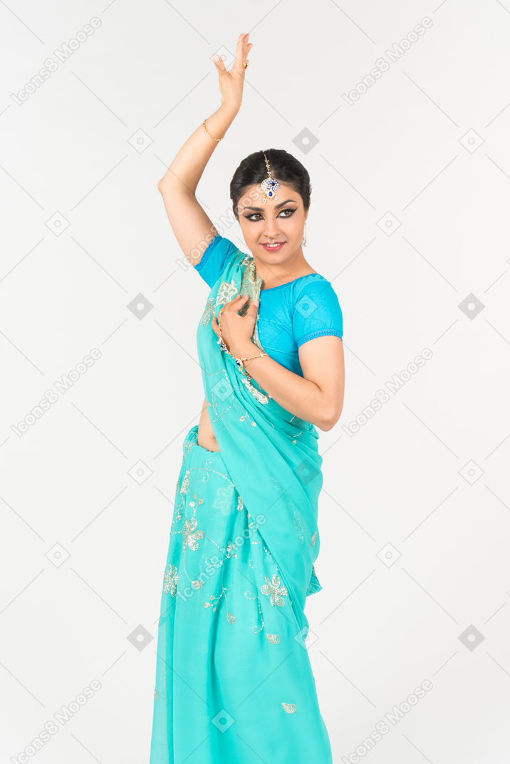 ダンスの位置に立っている青いサリーの若いインド人女性