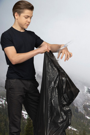 Young man throwing trash into a black trash bag