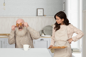 Hombre de edad cerrando los ojos con galletas y una mujer joven que lo mira