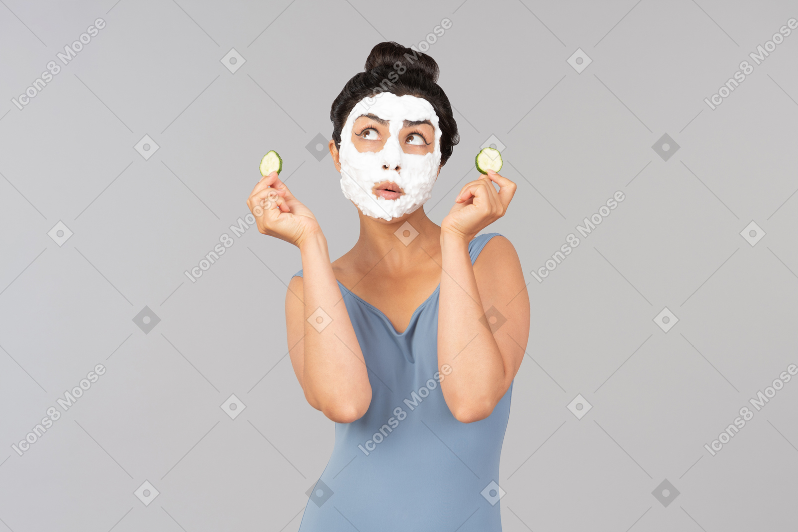 Woman with white facial mask holding cucumber slices